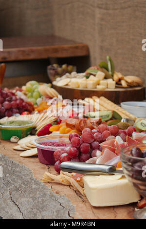 Eine helle und farbenfrohe Auswahl an Früchten, Nüssen, Käse, Dips, Wurst und Cracker über eine schöne Platte von Holz. Stockfoto