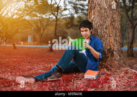 Junger Mann sitzen und ein Buch lesen im Park Stockfoto