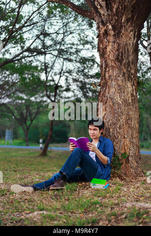 Junger Mann sitzen und ein Buch lesen im Park Stockfoto