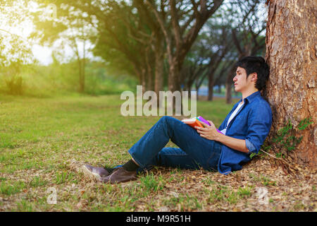 Junger Mann sitzt mit einem Buch in den Park Stockfoto