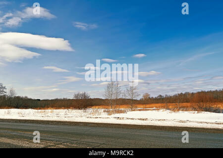 Ländliche Straße durch ein Feld der Schneeschmelze im Frühjahr Stockfoto