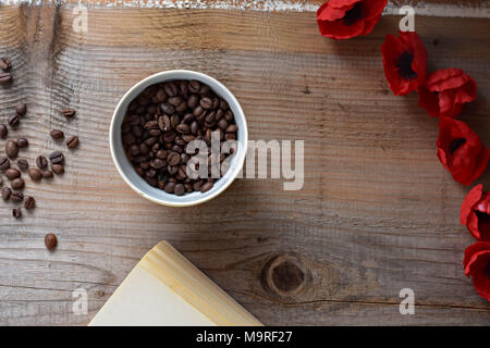 Kaffeebohnen, alte Buch und rote Blumen auf Holz- Hintergrund Stockfoto