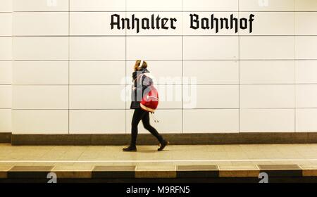 Eine junge Frau mit Kopfhörern geht am 16.02.2018 über einen Zugangsweg in der S-Bahnstation Anhalter Bahnhof in Berlin. Der Name der Station e in altdeutsche Schrift an der Wand. Foto: Wolfram Steinberg/dpa | Verwendung weltweit Stockfoto