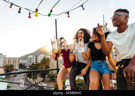 Multi-ethnischen Männer und eine Frau genießen und trinken während der Party auf dem Dach. Gruppe von jungen Freunden Spaß an der Terrasse. Stockfoto