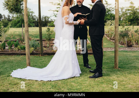 Paar stehend vor dem Priester für Hochzeit im Freien in den Park. Braut und Bräutigam stehen draußen in der Gegenwart der Priester während ihrer Stockfoto