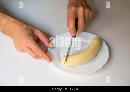 Des Menschen Hand schneiden eine Banane in eine Schüssel. Stockfoto