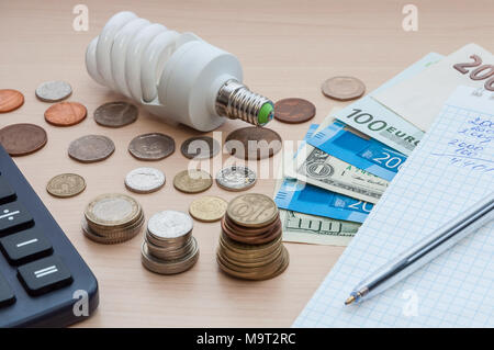 Eine Glühbirne, ein Notebook mit einem Stift, Rechnungen, verschiedenen Geld und einen Rechner auf dem Tisch. Stockfoto