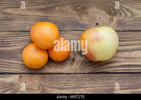 Vier helle orange reifen Mandarinen, einen Apfel und eine Schale mit einem Datum, das auf einem Holztisch. Stockfoto