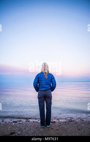 Eine Frau, die am Ufer bei Sonnenuntergang von hinten gesehen. Stockfoto