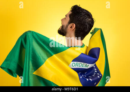 Brasilianischen Fußball-Fußball-Team Player. Ein Unterstützer und Ventilator holding Brasilien Flagge. Tragen gelbe Uniform auf gelben Hintergrund. Stockfoto