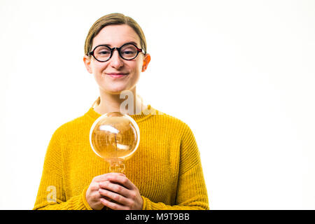 Inspiration und Kreativität - die Glühbirne Moment: Ein junger "geeky" Kaukasischen Frau Mädchen mit einem gelben Pullover Pullover und der runden Brille, mit einem alten Retro-Stil elektrischen Glühbirne, vor einem weißen Hintergrund, Großbritannien Stockfoto