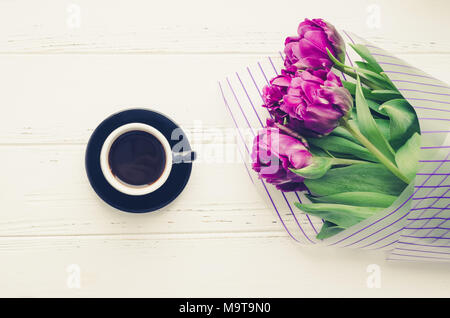 Tasse Kaffee am Morgen und Blumenstrauß der Frühling Blumen Tulpen über weiß Holz- Hintergrund. Ansicht von oben. Morgen Grußkarte. Urlaub, Romantik der modernen l Stockfoto