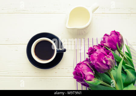 Tasse Kaffee, Milch und Blumenstrauß der Frühling Blumen Tulpen über weiß Holz- Hintergrund. Ansicht von oben. Morgen Grußkarte. Urlaub, Romantik der Mo Stockfoto