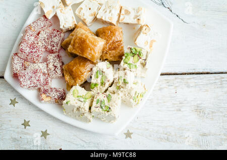 Verschiedene traditionelle östliche Desserts auf weißem Holz- Hintergrund. Baklava, Halva, rahat Lokum, Sorbet, Nüsse, Datteln, kadayif auf Platten. Ansicht von oben. Co Stockfoto