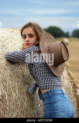 Junges Mädchen mit Cowboyhut lehnte sich auf Heu Brötchen, Yorkshire, Großbritannien Stockfoto