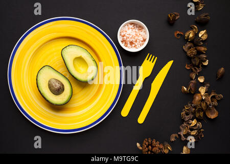 Einzelne, geschnittene Avocado auf gelbem Schild. Aufnahme von oben nach unten. Mitglied der Lauraceae Familie. Stockfoto