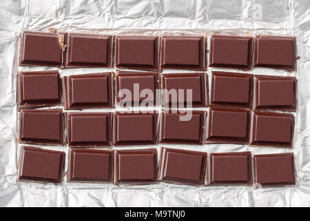 In Stücke von Dark Chocolate Bar in der metallfolie Verpackung gequetscht werden. Stockfoto