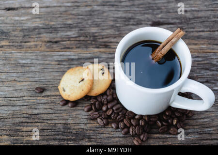 Heißer Kaffee in weiße Tasse mit Kaffeebohnen und Cookies auf Holz Hintergrund Stockfoto