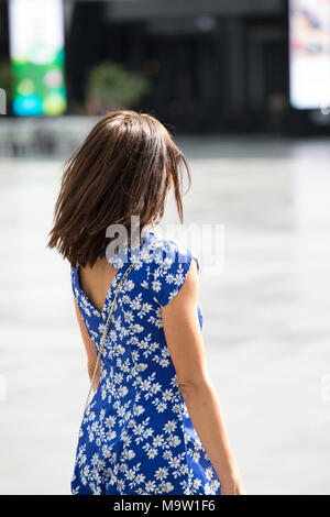 Rückansicht einer Frau tragen Blur geblümten Kleid zu Fuß auf der Straße Stockfoto