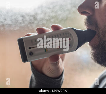 Mann in ein Peak Flow Meter bei Asthma Schweregrad zu prüfen. Stockfoto