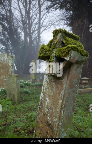 Ein Stein Keltisches Kreuz Grabstein mit Moos und Flechten auf einem nebligen Winter morgen, All Saints Church, Holdenby, Northamptonshire, England. Stockfoto