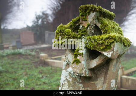 Ein Stein Keltisches Kreuz Grabstein mit Moos und Flechten auf einem nebligen Winter morgen, All Saints Church, Holdenby, Northamptonshire, England. Stockfoto