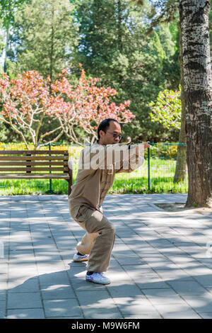 Ein Chinese, der ein traditionelles Kostüm der Kampfkunst trägt, übt Tai Chi im Tiantan-Park, in der Nähe des Himmelstempels, Peking, China Stockfoto