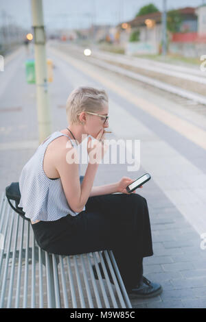 Junge Frau sitzt im Freien mit smart phone Hand halten - Technologie, soziales Netzwerk, Kommunikation Konzept Stockfoto