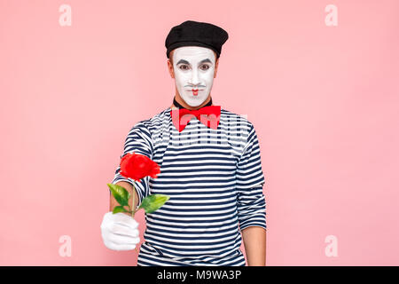 Closeup Portrait von stattlicher Mann vorhanden rote Rose für Sie. Clown, Artist, Mime. Studio shot, rosa Hintergrund Stockfoto