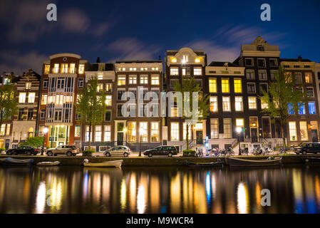 Schöne Nacht in Amsterdam. Nacht Beleuchtung von Gebäuden und Boote in der Nähe der Wasser in den Kanal. Stockfoto