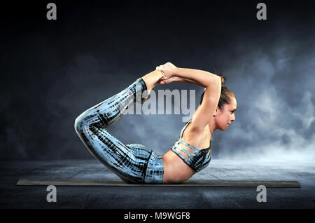 Athletische Frau Demonstration der Bogen im Yoga in einer Nahaufnahme Seite Blick auf einem schwarzen Hintergrund mit Rauch Stockfoto