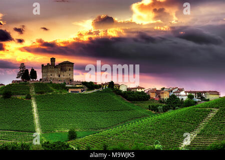 Ein spektakulärer Sonnenuntergang Himmel überragt das Dorf Grinzane Cavour mit seinem Schloss (Unesco W. H.S.) durch die Weinberge der Langhe, Piemont umgeben. Stockfoto