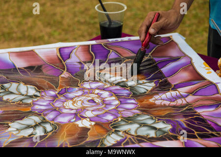 Nahaufnahme eines Malaysischen batik Handwerker zeigen, wie man Pinsel Farbe Farben auf einen Stoff mit dem beliebten Motiv der Blätter und Blüten. Stockfoto