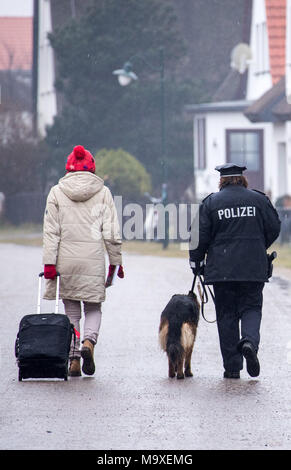 13 März 2018, Deutschland, Hiddensee: Insel Polizeioffizier Martina Dominik und ihr Deutscher Schäferhund Maggie zu Fuß neben einem Urlauber in der Stadt von Vitte auf der Ostseeinsel Hiddensee. Dominik arbeitet seit dem vergangenen Jahr Als einzige Polizeioffizier, dort, wo die meisten Leute ihren Urlaub nehmen. Vor allem im Sommer, wenn Tausende von Touristen strömen in der Insel gibt es eine Menge Arbeit betreut werden, einschließlich Verkehr Verletzungen, um Störungen und kleinen Diebstählen. Foto: Jens Büttner/dpa-Zentralbild/dpa Stockfoto