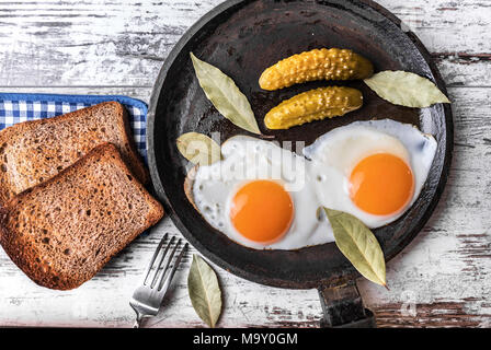 Spiegelei in der Pfanne. Roggen Toast und Gurken neben Spiegeleier. Stockfoto