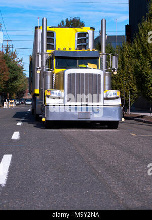 Leuchtend gelbe American Classic Big Rig halb LKW-Flotte mit Gefrierfach Auflieger und hohen verchromte Auspuffrohre von Urban city Street laufen für timel Stockfoto