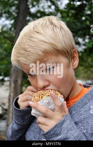 Blonde Junge mit großen Bissen in Erdnuss abgedeckt caramel Apple außerhalb im Herbst am historischen 1837 Franklin Cider Mill, Bloomfield Hills, Michigan, USA. Stockfoto