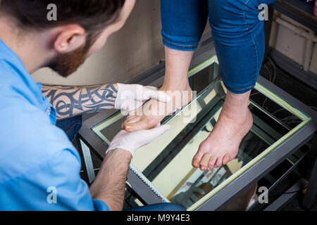 Die hände eines jungen Mannes Arzt Orthopäde führt Diagnose, Fuß Fuß Test einer Frau, die für die Herstellung von individuellen, orthopädische Einlagen Stockfoto