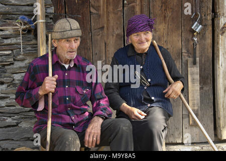 Ein älteres Paar holding Walking Stöcke auf eine Bank außerhalb eines alten Stein vergießen, Harderwijk, obere Swanetien, Georgien rest Stockfoto