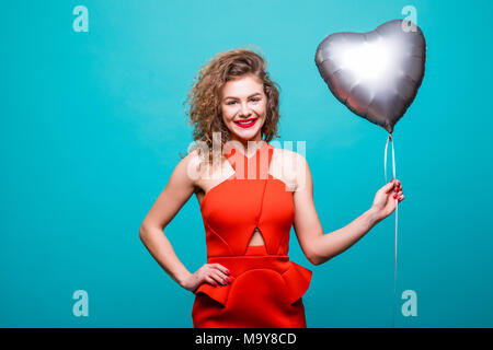 In voller Länge Bild der wunderschönen Frau in Fancy red Outfit vor der Kamera mit Herz Form ballon Posing, über grüne Wand isoliert Stockfoto