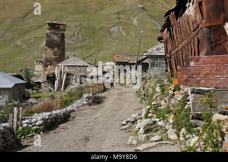 Ein mittelalterlicher Wehrturm und alten Häuser stehen entlang einer Straße in das Dorf Ushguli, obere Swanetien, Georgien Stockfoto