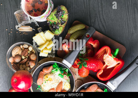 Gesundheit Frühstück. Spiegeleier mit Würste in einer Pfanne mit Gewürzen und frischem Gemüse, Käse, Nüsse, Avokado, Sandwich mit Avokado und Basilikum Stockfoto