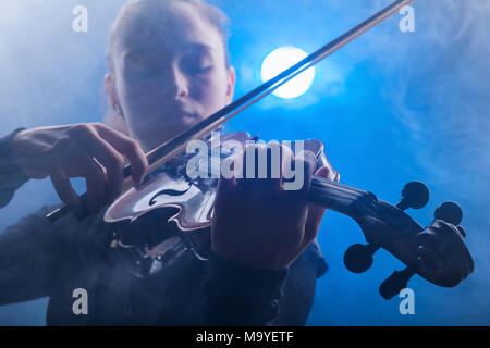 Frau Spielen der Violine vor einem dunklen Hintergrund. Nebel im Hintergrund. Studio shot Stockfoto