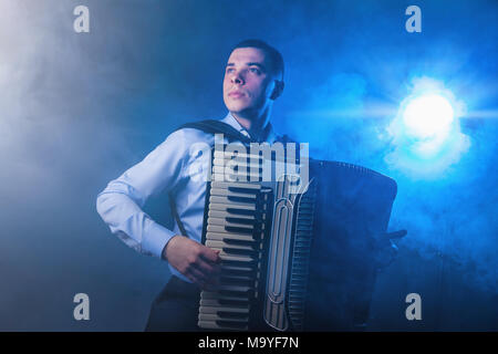 Musiker spielen auf dem Akkordeon vor einem schwarzen Hintergrund. Nebel im Hintergrund. Studio shot Stockfoto