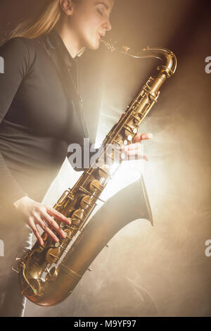 Saxophonist. Frau mit Saxophon auf einem beigen Hintergrund. Nebel im Hintergrund. Studio shot Stockfoto