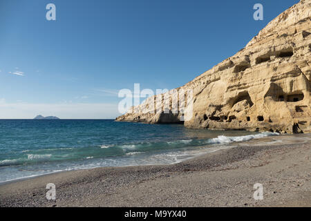 Strand von Matala mit Felsen und Höhlen und eine kleine Insel in der Ferne Stockfoto