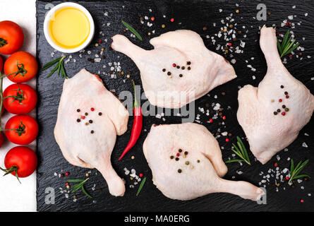 Rohes Geflügelfleisch. Entenschenkel mit Rosmarin, Gewürze, Gemüse und Olivenöl auf schwarzem Hintergrund, Ansicht von oben Stockfoto