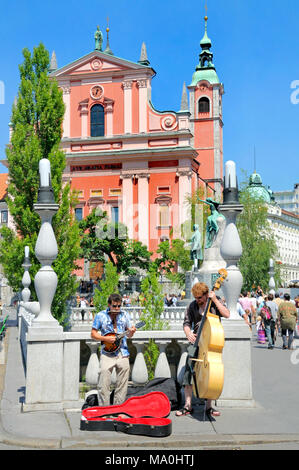 Ljubljana, Slowenien. Gaukler auf der Tromostovje (Triple Bridge) in Fron der Franziskaner Kirche der Mariä Verkündigung Stockfoto