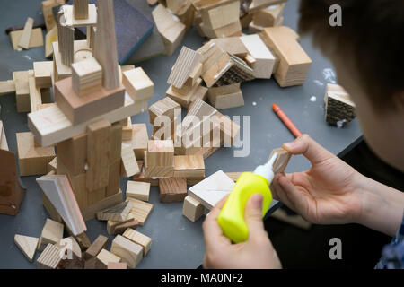 Nahaufnahmen der Hände des Kindes spielen mit Holz- Konstruktor, Ziegel auf Tisch. Junge Leime Bausteine Haus, Gebäude Stockfoto