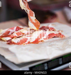 Nahaufnahme der dünne Scheiben Prosciutto Crudo, italienischer Schinken Gewicht auf die Waage im Lebensmittelgeschäft. Realen Szene im Supermarkt, Store organische Produkte Stockfoto